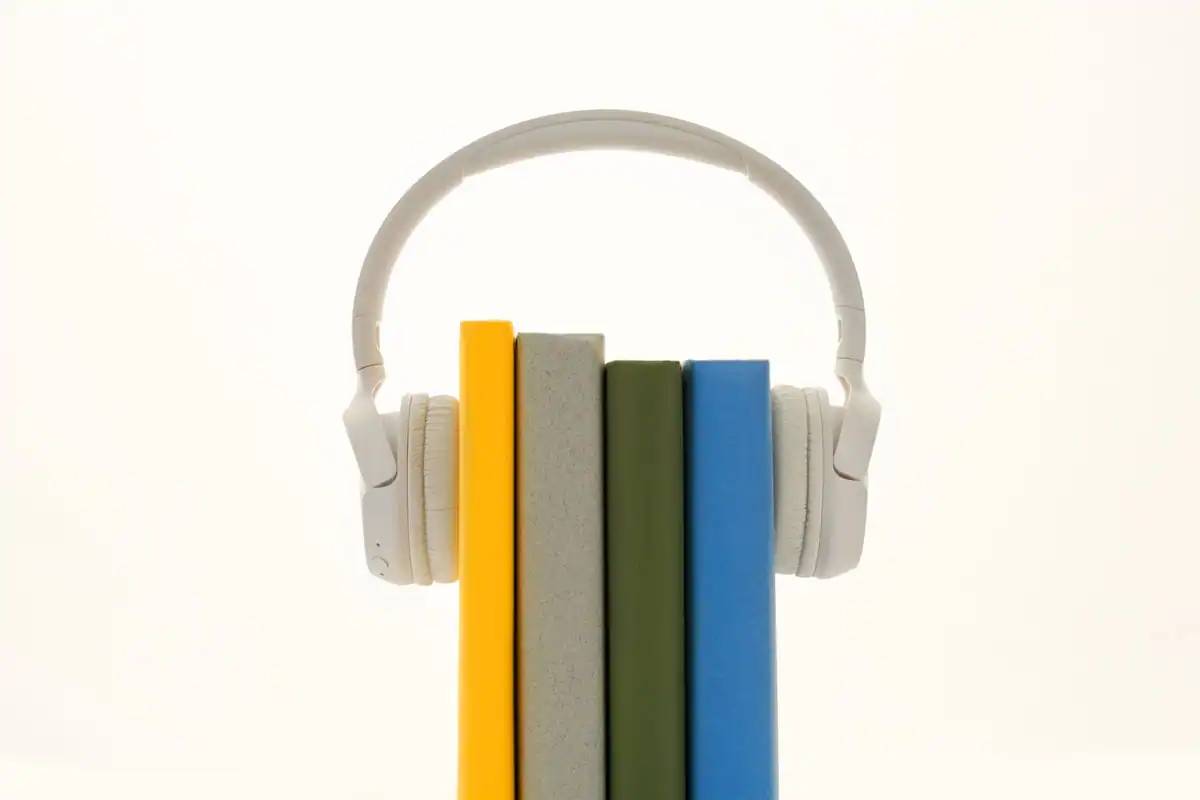 Căști albe puse peste un șir de cărți colorate, simbol pentru ascultarea audiobookurilor