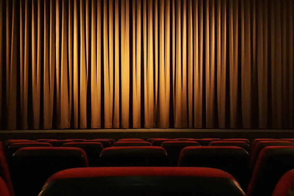 Cortină aurie de scenă și rânduri de scaune roșii într-o sală de teatru goală