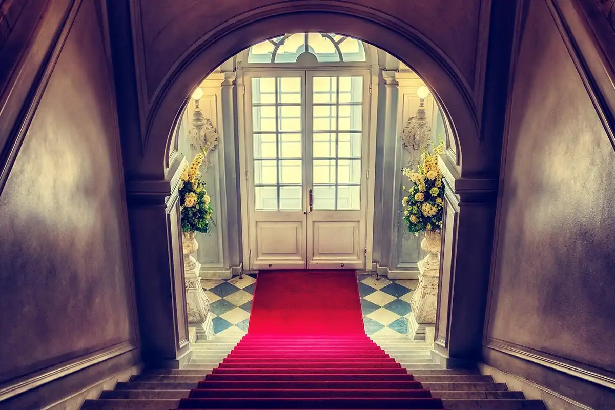 Scară acoperită cu covor roșu, care duce spre o ușă arcuită, luminată, a unui teatru