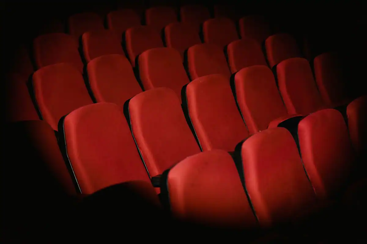 Rânduri de fotolii roșii goale într-o sală de cinema slab luminată
