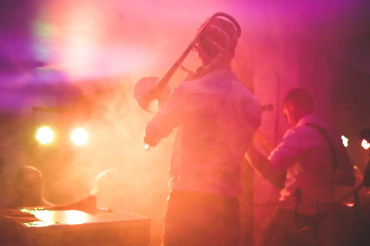 Un trombonist cântă pe scenă, învăluit în fum și lumini roz și portocalii