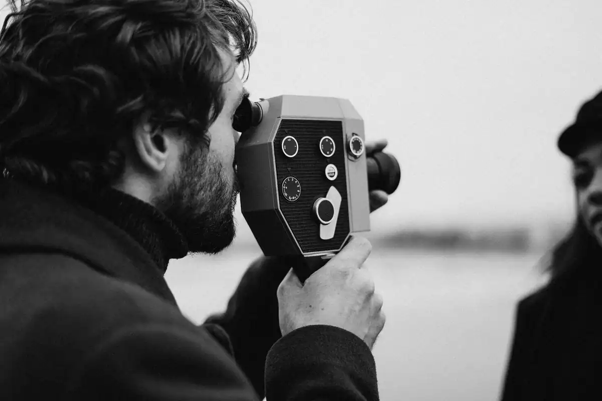 Un bărbat filmează cu o cameră veche de film, într-o fotografie alb-negru