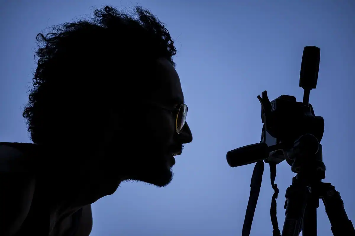 Siluetă a unui bărbat cu cameră de filmat pe trepied, pe fundal albastru