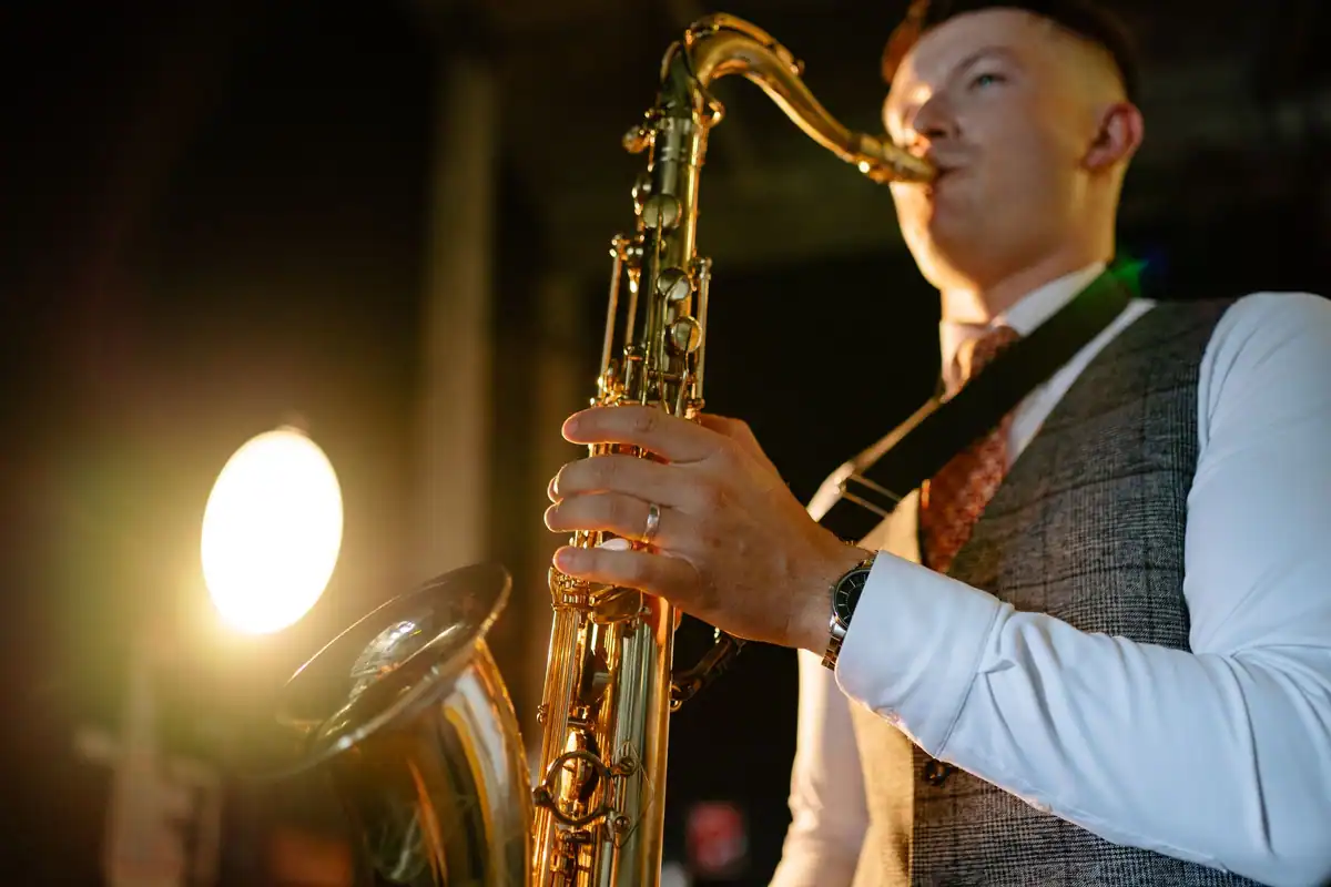 Un saxofonist cântă sub o lumină caldă de scenă, în cămașă și vestă