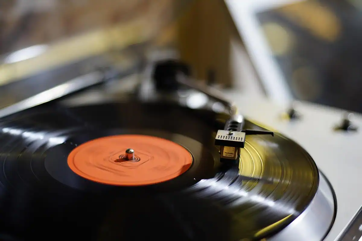Disc de vinil cu eticheta portocalie rotindu-se pe un pick-up, văzut de aproape