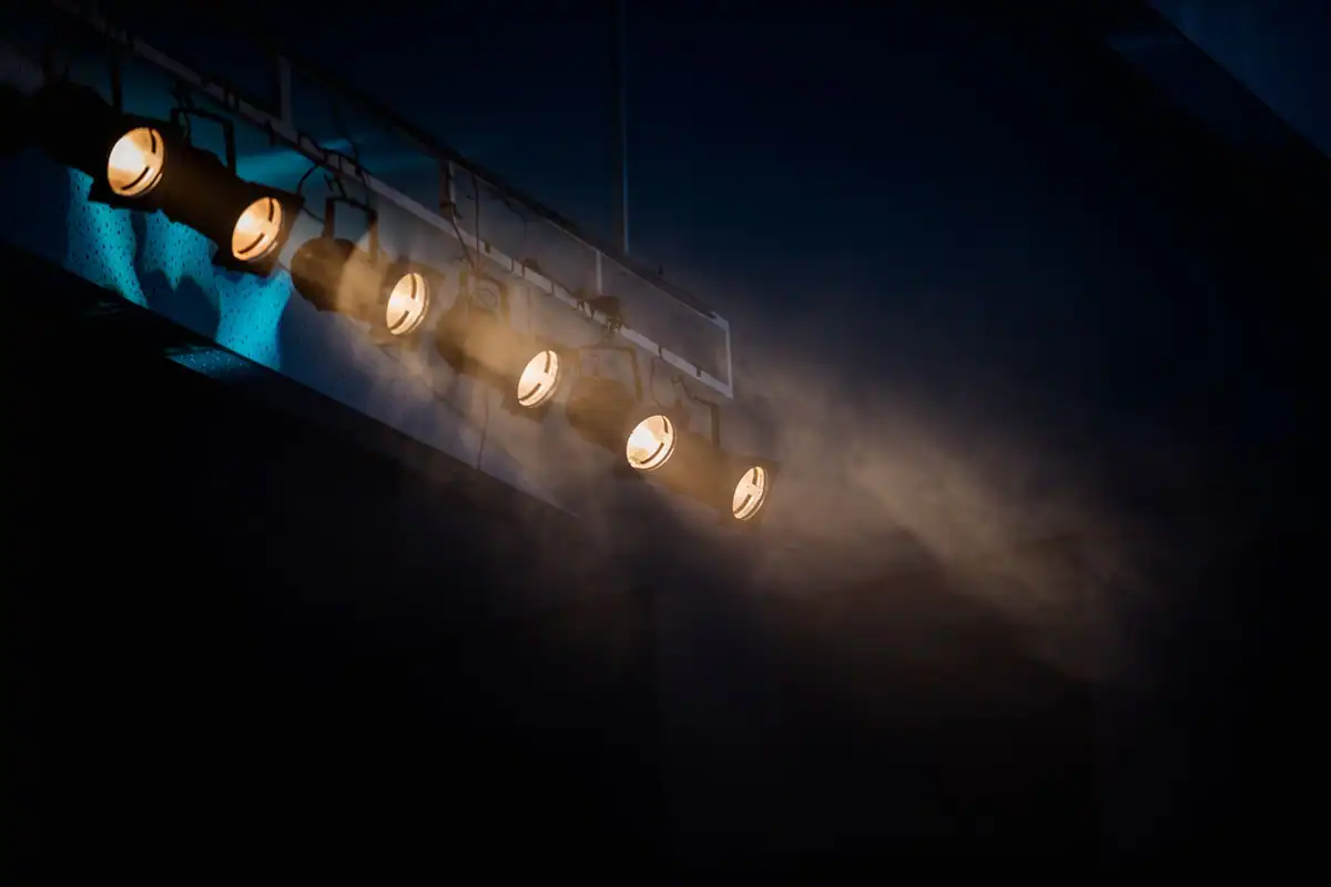 Reflectoare de scenă aliniate pe o bară, cu fascicule de lumină în întuneric