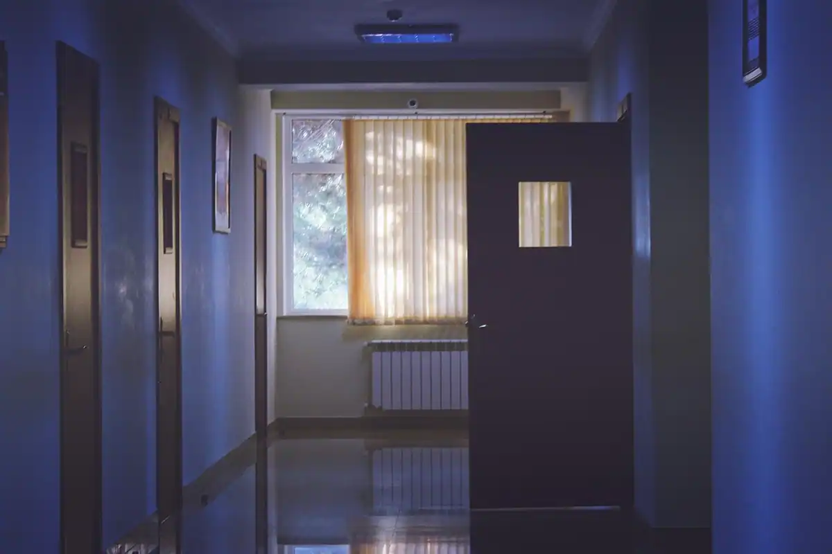 Coridor de spital cu pereți albaștri, uși închise și o fereastră la capăt