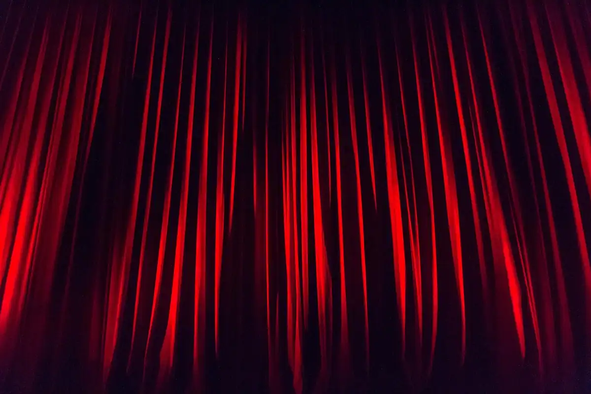 Cortină roșie de scenă, cu falduri lungi, luminată dintr-o parte