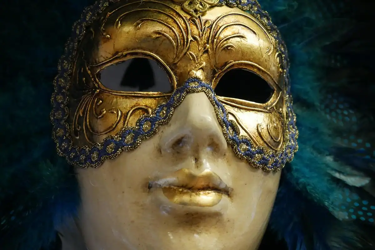 Mască venețiană aurie, decorată cu ornamente fine, fotografiată din față, pe fundal închis