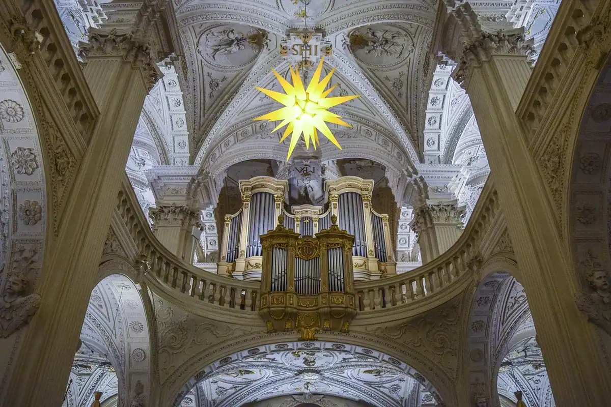 Orgă cu tuburi într-o biserică barocă, sub bolți albe cu decorații aurii