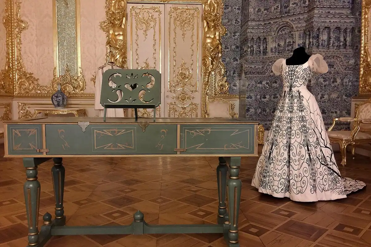 Clavecin într-o sală de palat cu pereți aurii, lângă o rochie de epocă