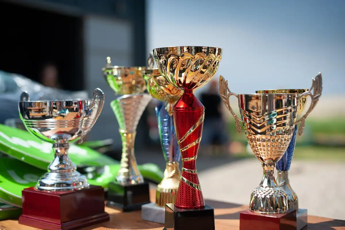 Mai multe cupe și trofee strălucitoare pentru câștigători, așezate pe o masă