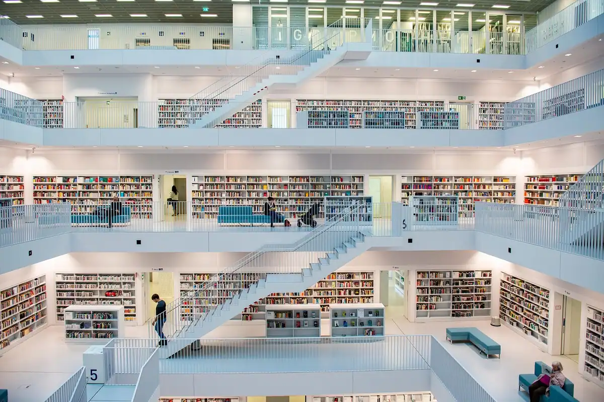 Atriu luminos al unei biblioteci moderne, cu mai multe etaje de rafturi și scări albe