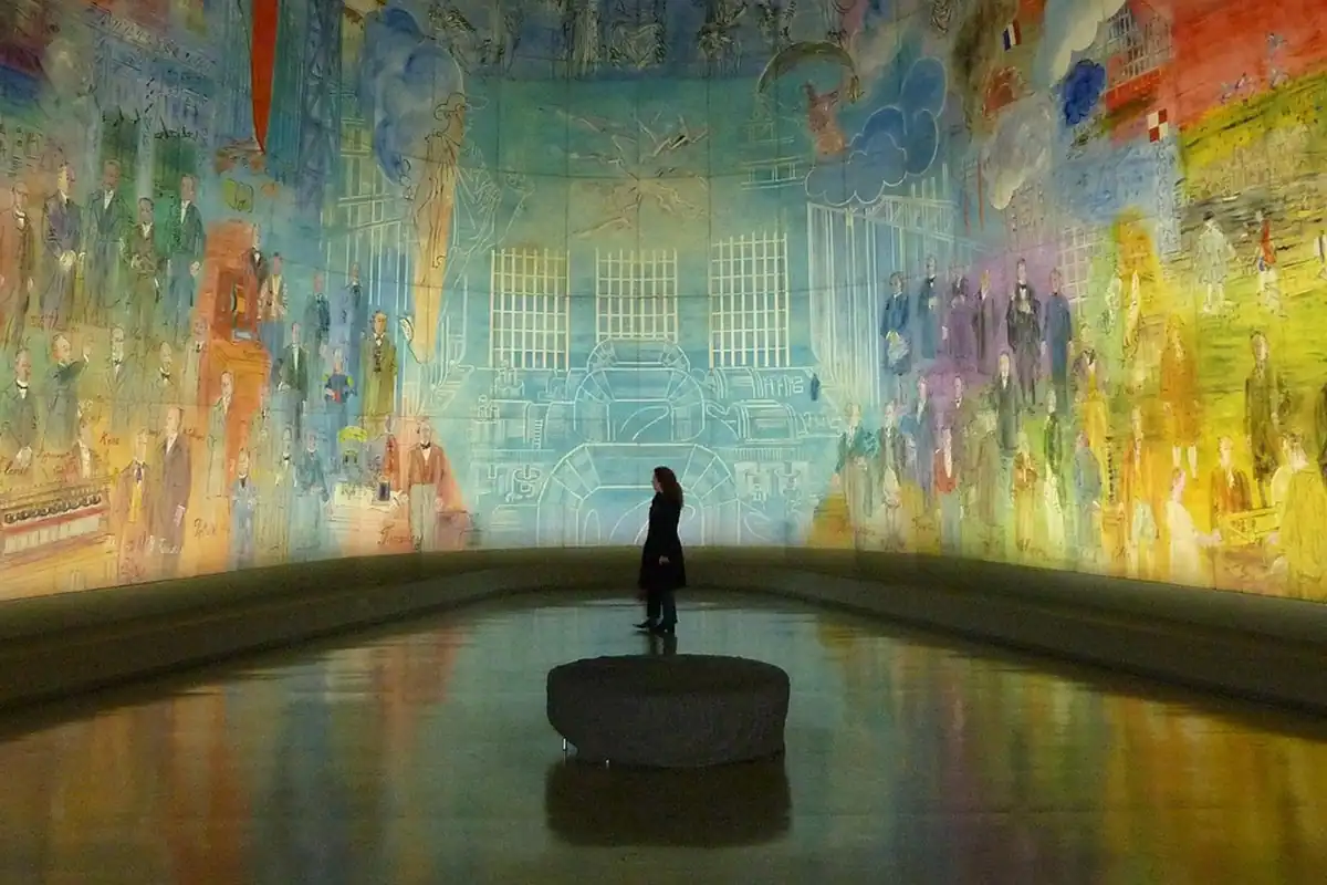 O siluetă stă în fața unei picturi murale uriașe și colorate, într-o sală de muzeu