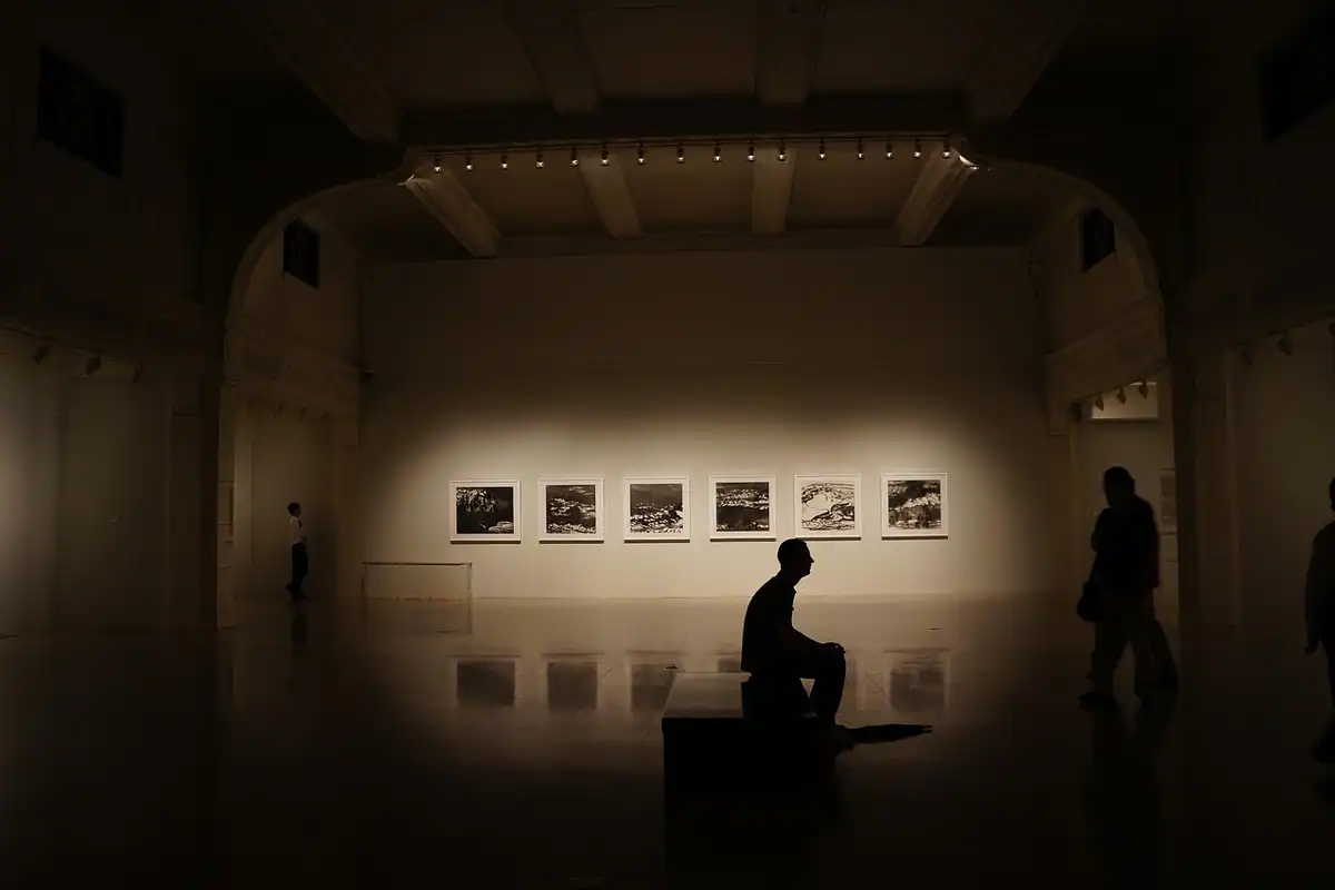 Vizitator așezat pe un scaun într-o galerie întunecată cu fotografii pe perete